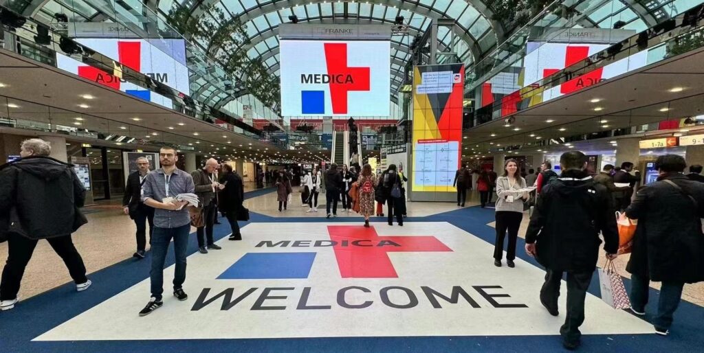 Entrance area of MEDICA 2025 trade fair in Düsseldorf with visitors entering the exhibition.
